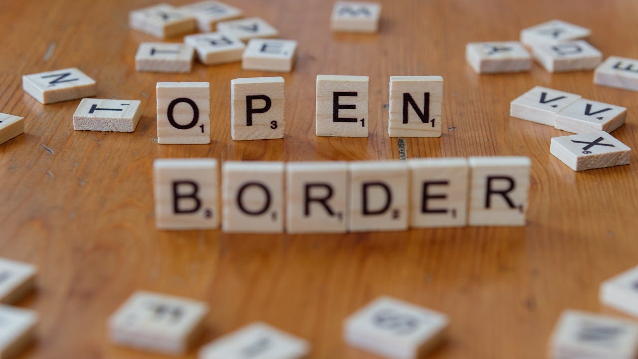 Wooden Scrabble letters on a table spelling out open border, concept of migration and geopolitics.